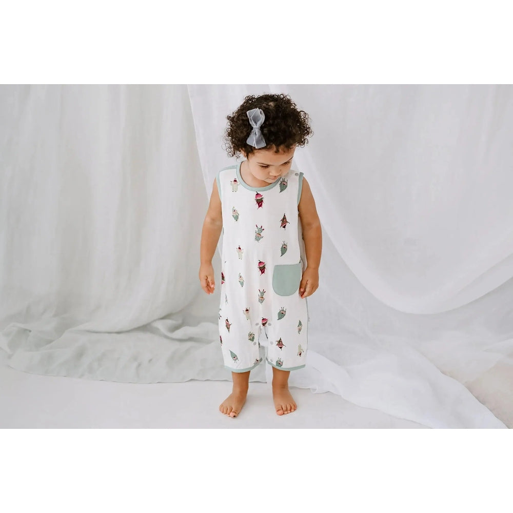 Nest Designs Bamboo Sleeveless Romper Pixie Dust, white with pastel cactus print, blue trim and pocket; baby stands barefoot.