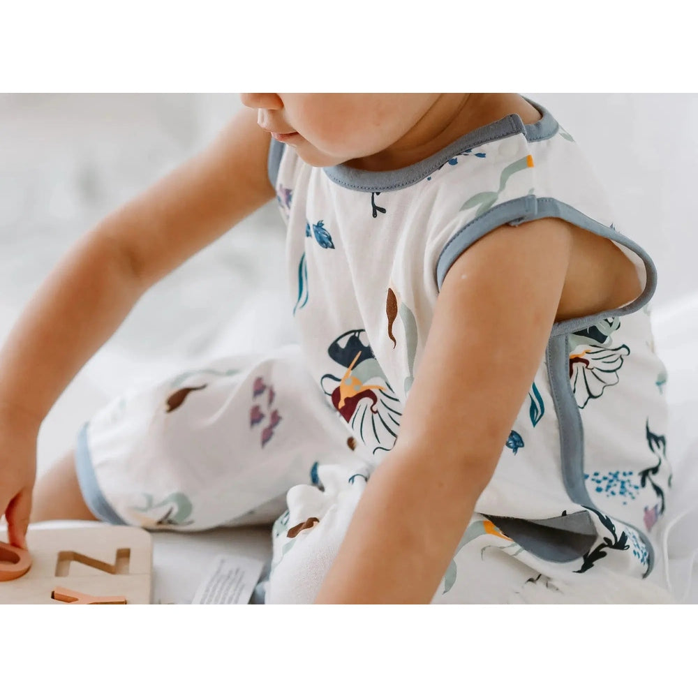 Nest Designs Bamboo Sleeveless Romper Splish Splash in white with ocean print and gray trim, baby reaching for blocks.