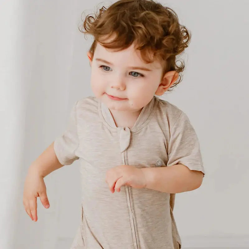 Nest Designs Basics bamboo cotton short-sleeve drop-bottom romper in warm taupe, toddler playing and moving his arms.