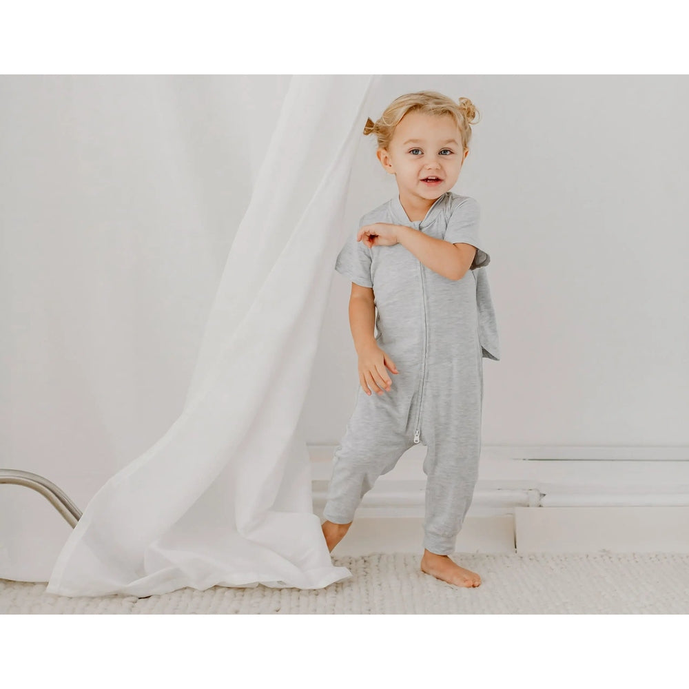 Nest Designs Basics Bamboo Cotton Short Sleeve Drop Bottom Romper Grey Dawn; toddler stands barefoot, gripping the front zipper.