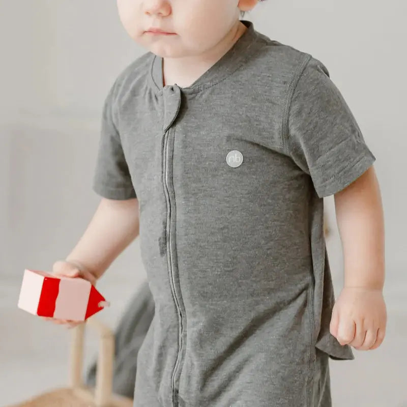 Nest Designs Basics Bamboo Cotton Short Sleeve Drop Bottom Romper Charcoal; baby in grey romper lifts a red block toy.