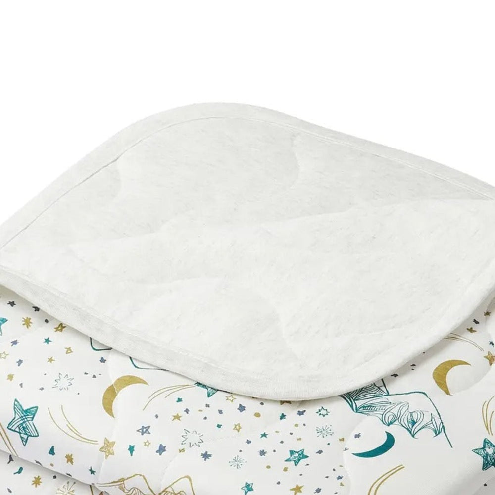 Nest Designs Cozy Blanket Small Stars White folded on a starry bedspread, showcasing soft white fabric.