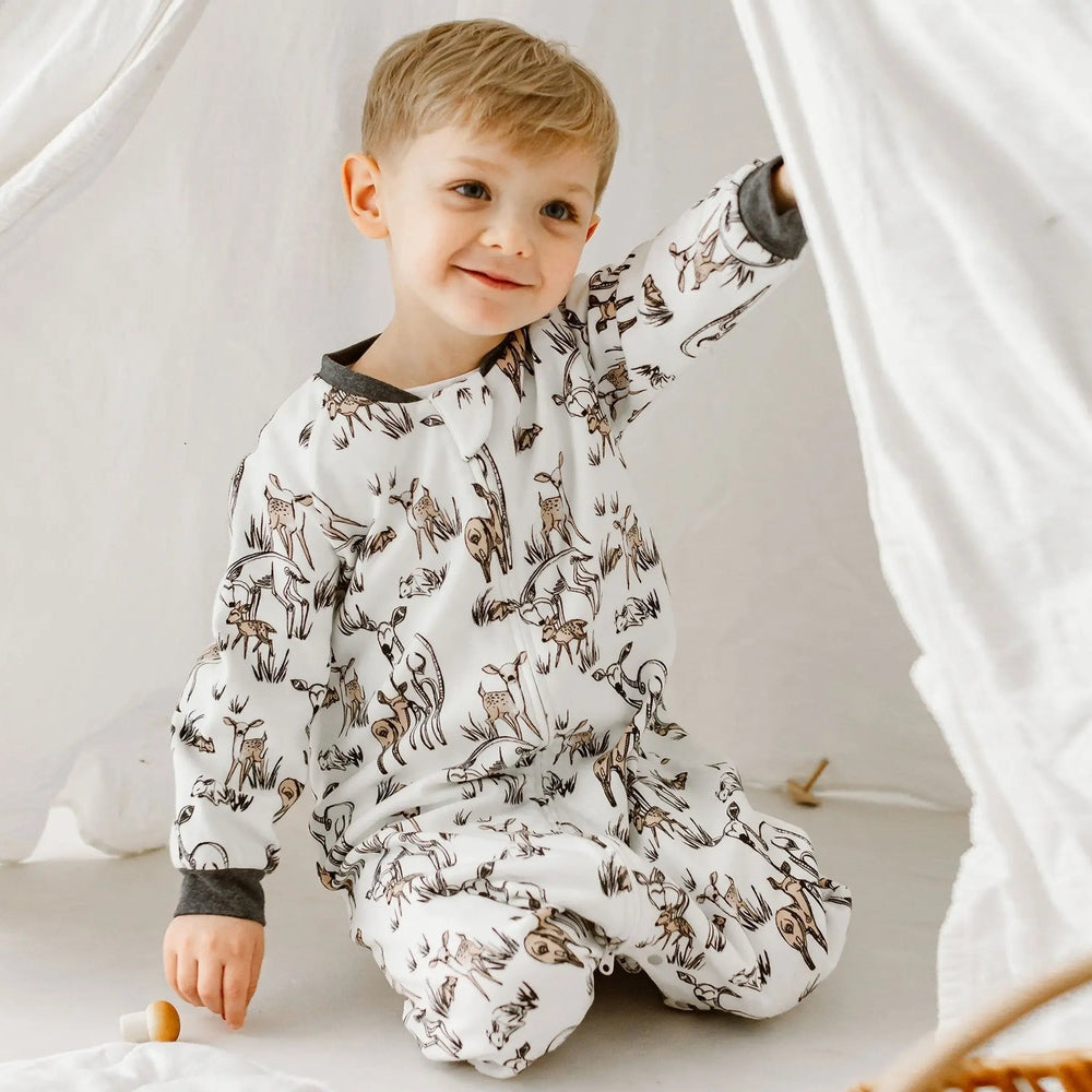 Nest Designs Organic Cotton Long Sleeve Sleep Suit 1.0 Tog Mama Deerest; smiling boy pulls aside a white canopy in a deer-print pajama set.