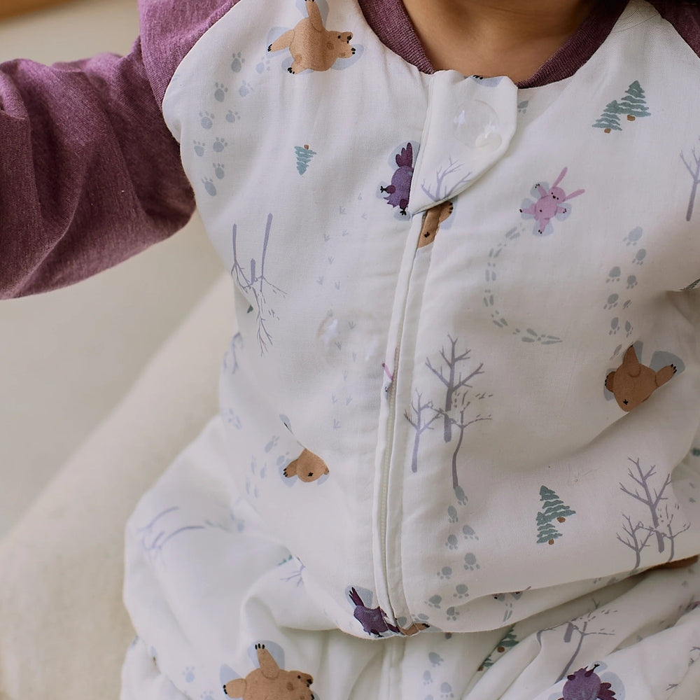 Nest Designs Raglan Bamboo Long Sleeve Footed Sleep Bag 2.5 Tog Snowy Angels worn by baby, with a front zipper and maroon sleeves visible.