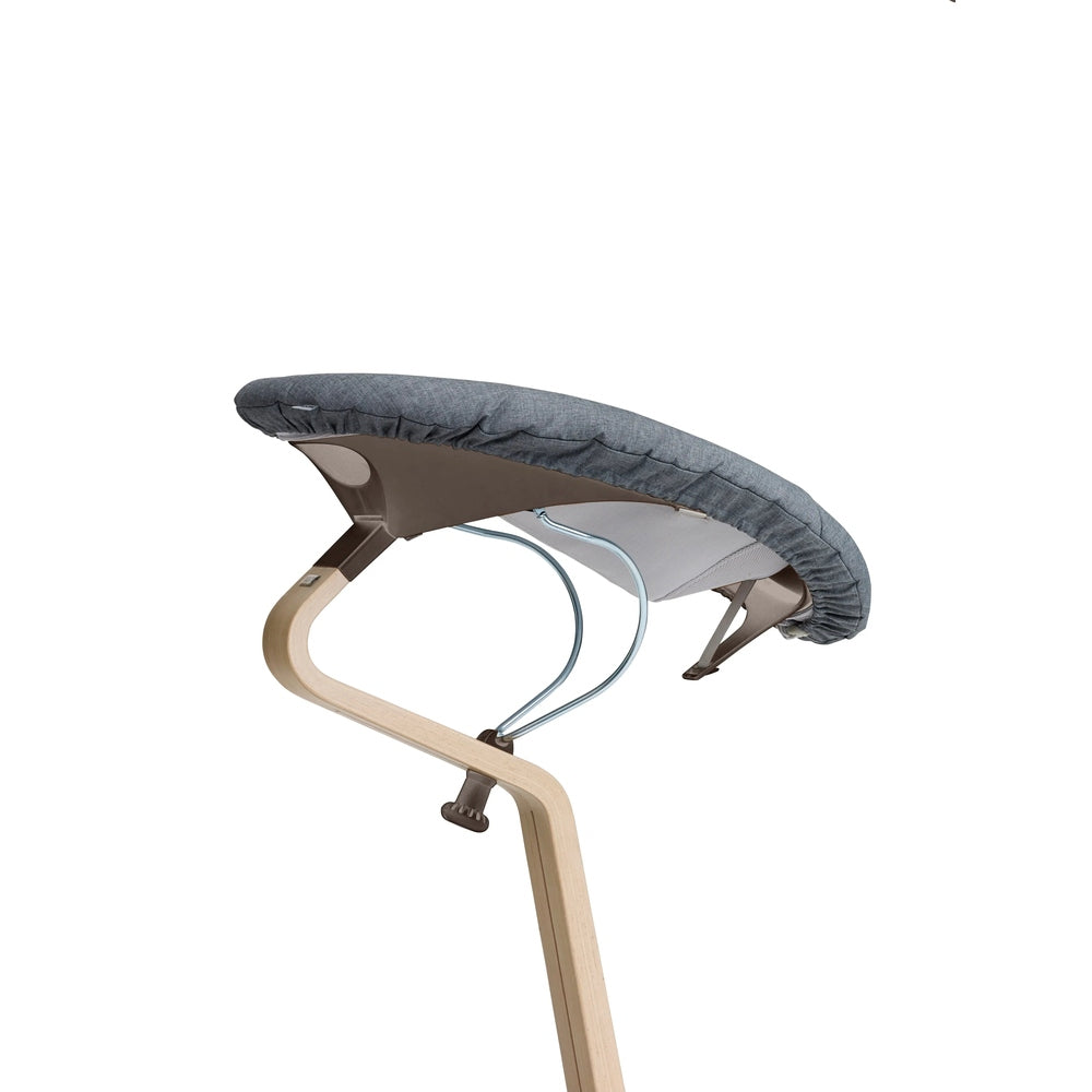 NOMI Baby high chair cushion in gray fabric attached to a light wood frame with metal supports.
