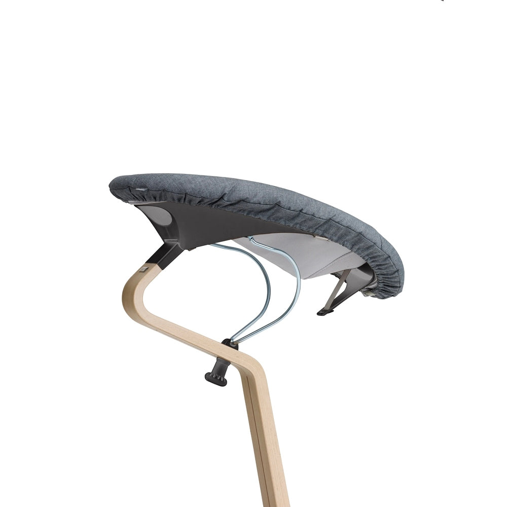 NOMI Baby high chair cushion in grey fabric, secured to curved wooden leg frame with metal supports.