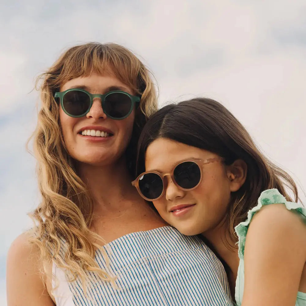 Olivio & Co Oval Sunglasses Junior+ Classic Olivio Sand Beige worn by two girls posing in sunlight with dark lenses.