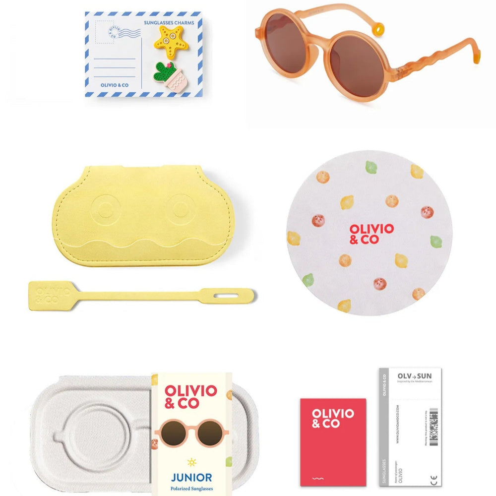 OLIVIO & CO Round Sunglasses Kids Citrus Garden Grapefruit Pink set, shown with yellow case and accessories arranged around the round-framed sunglasses.