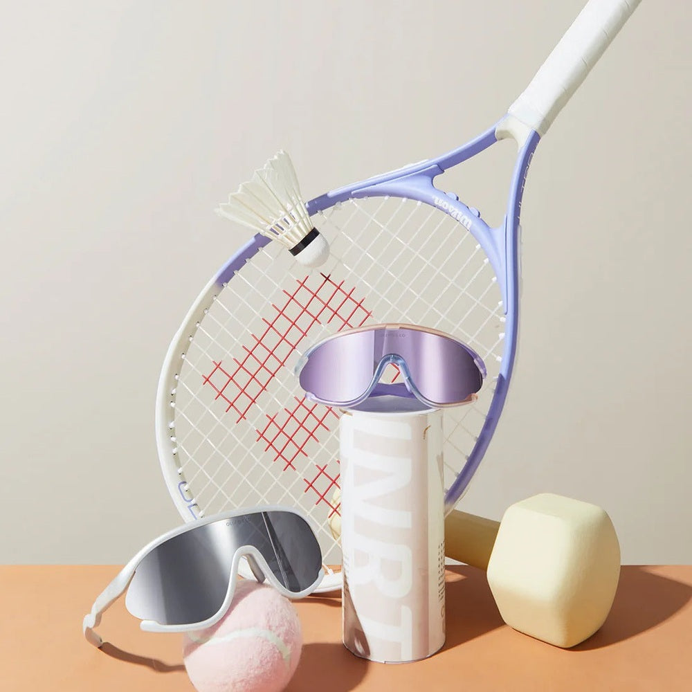 Olivio & Co Sport Sunglasses Kids Ocean Fantasy, full-rim purple mirrored lenses resting on a bottle among sporty gear.