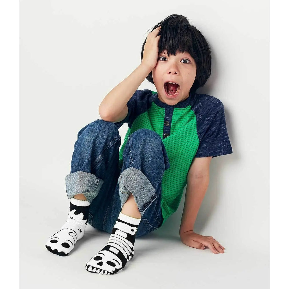 Pals Socks Glow In The Dark Ghost & Skeleton Kids Mismatched; child sits, showing one ghost and one skull sock.
