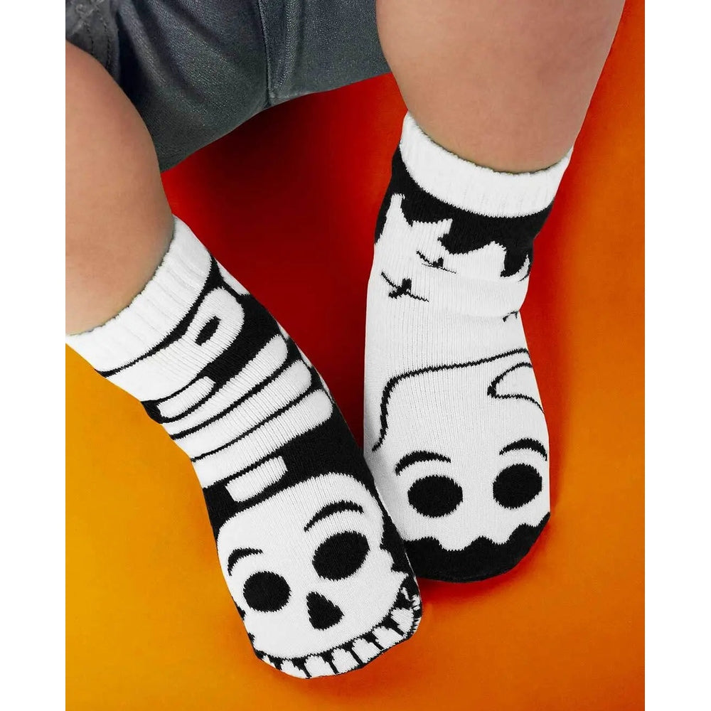 PALS SOCKS Glow In The Dark Ghost & Skeleton Kids Socks, mismatched white with black skull toes, feet resting on orange.