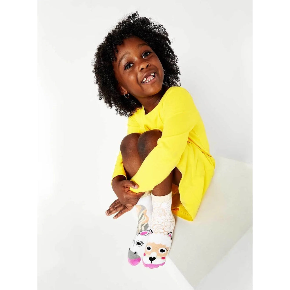 Pals Socks Horse & Alpaca mismatched kids socks; white with animal faces, worn by a smiling child in a yellow dress.