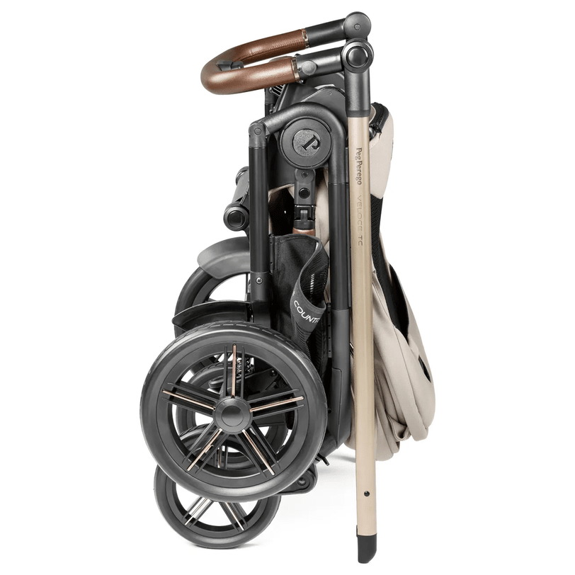 Peg Perego Velcoe TC Stroller folded compactly with beige fabric, black frame and tan leather handle.