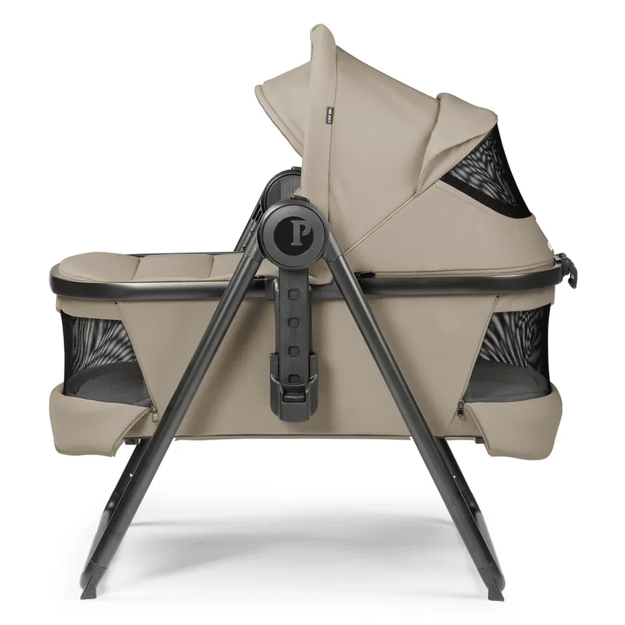 Peg Perego YPSI Bassinet with Stand by Me in beige; sturdy gray frame supports the bassinet with mesh side panels.