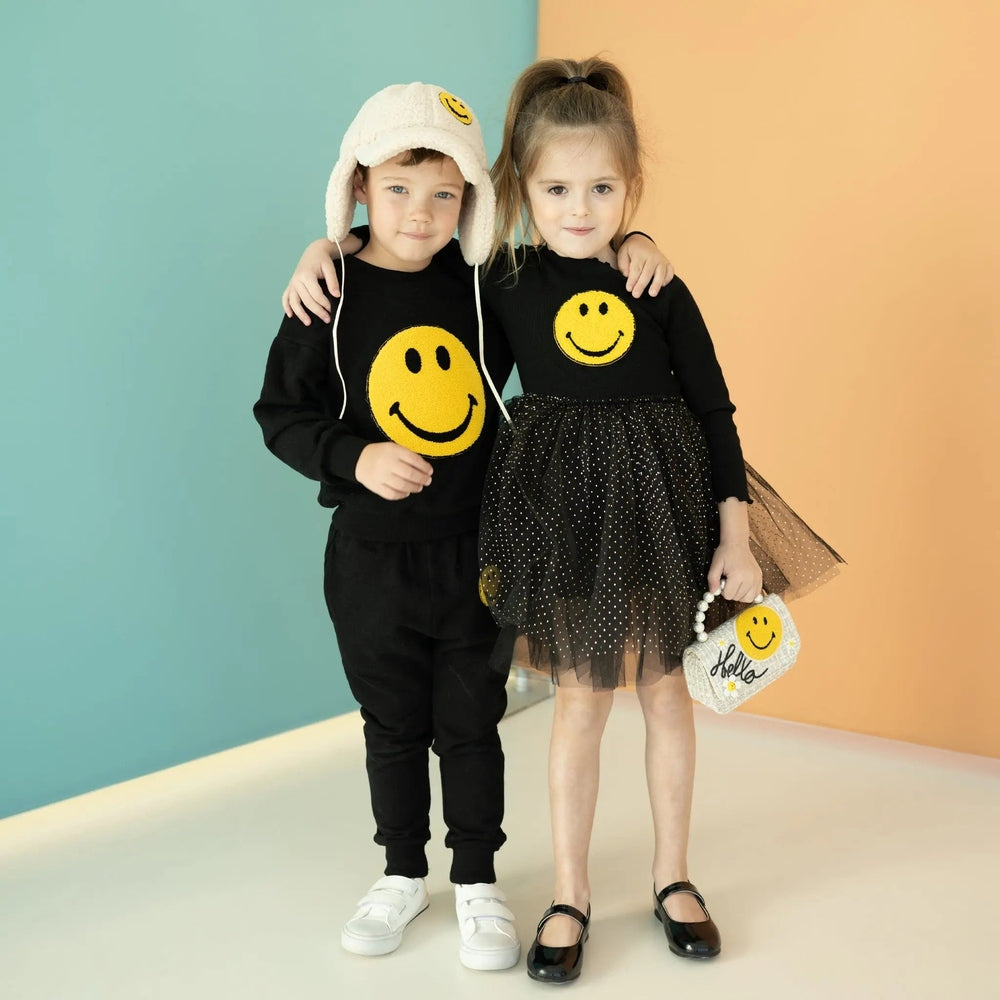Petite Hailey Smile Tutu Black: playful duo in matching black outfits with yellow smiley, girl in dotted tulle tutu holding a smiley bag.