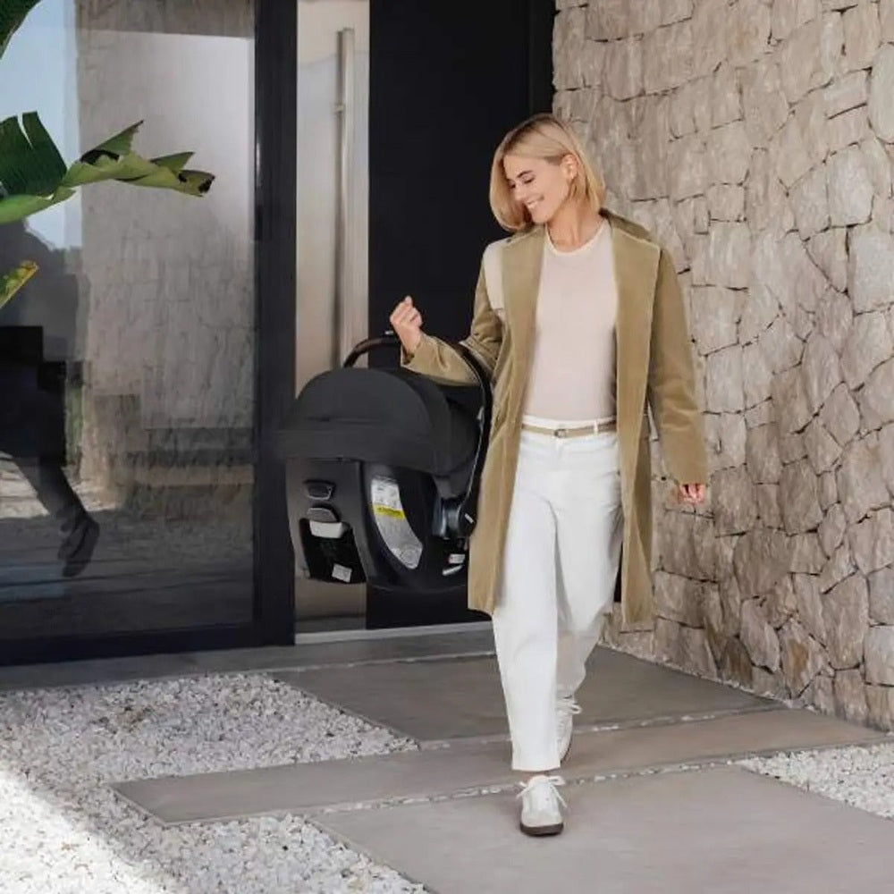 Romer Juni Infant Car Seat with Versa Base by ROMER, woman in a beige trench carries the car seat by its handle.