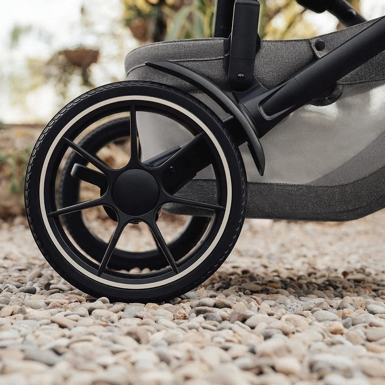 ROMER Tura Stroller close-up of black alloy wheel rolling on pebbles, highlighting outdoor-ready full-sized design.