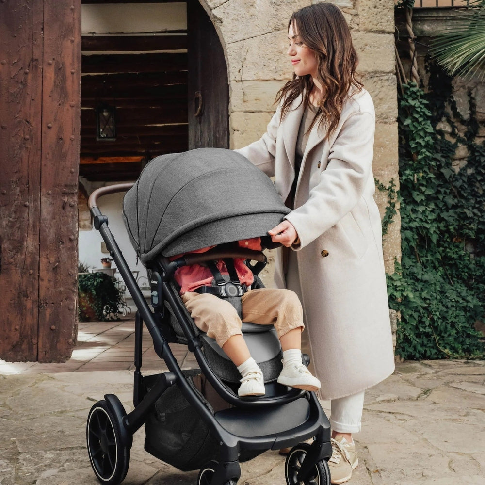 Romer Tura Stroller in gray canopy; toddler seated as mom pushes the full-sized stroller outdoors.