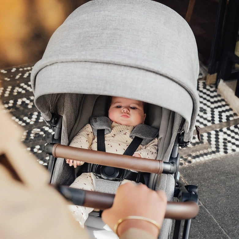 Romer Tura Stroller in light grey with brown handle, baby secured in harness while pushed.
