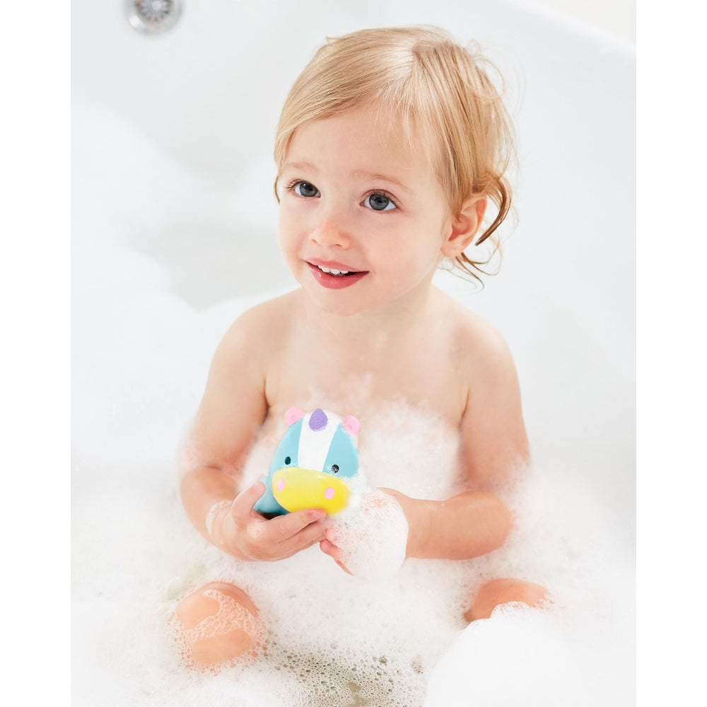 Skip Hop Zoo light-up unicorn bath toy in blue, held by smiling toddler in bubbly bath