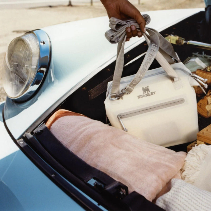 Stanley white cooler bag with gray straps and a front zipper pocket being carried from a car trunk.