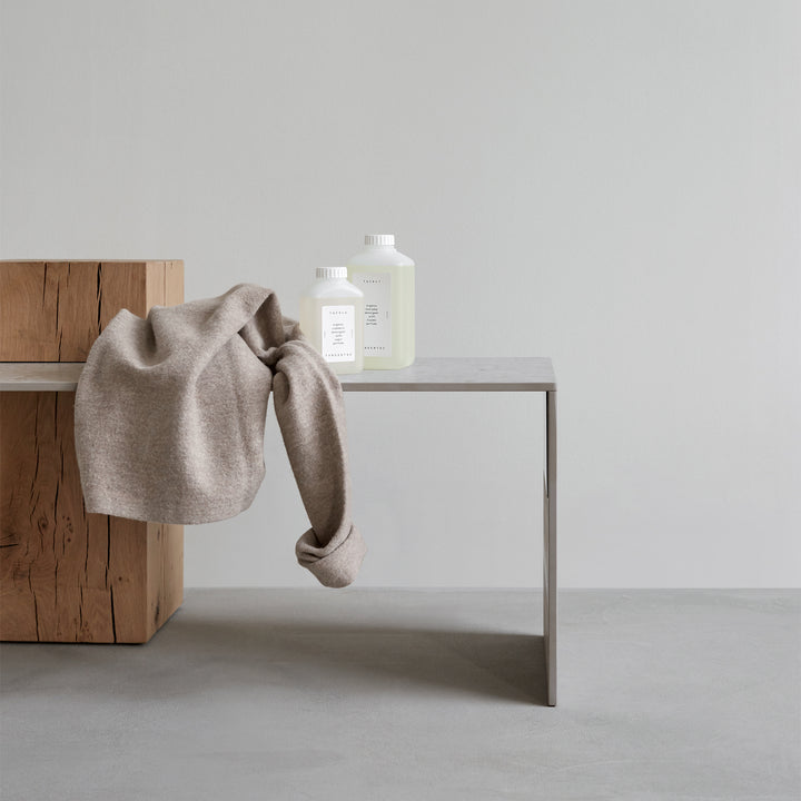 Tangentgc Kiyomi fabric softener bottles (2) on gray table with a beige blanket draped nearby