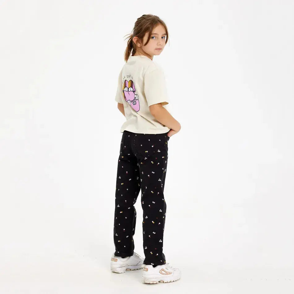 The New Halat-Shirt White Swan worn by a girl in a cream tee with back graphic, black floral pants, white sneakers