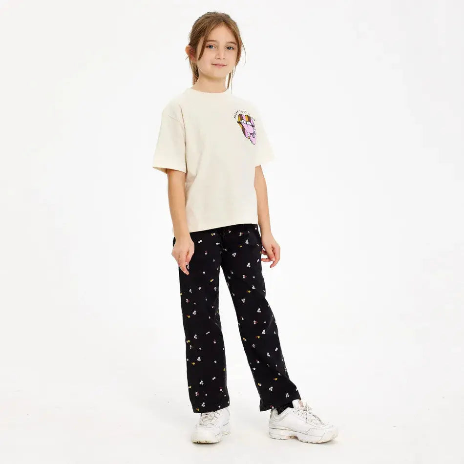 The New Halat-Shirt White Swan cream tee with pink graphic, worn by a girl standing in black patterned pants and white sneakers.