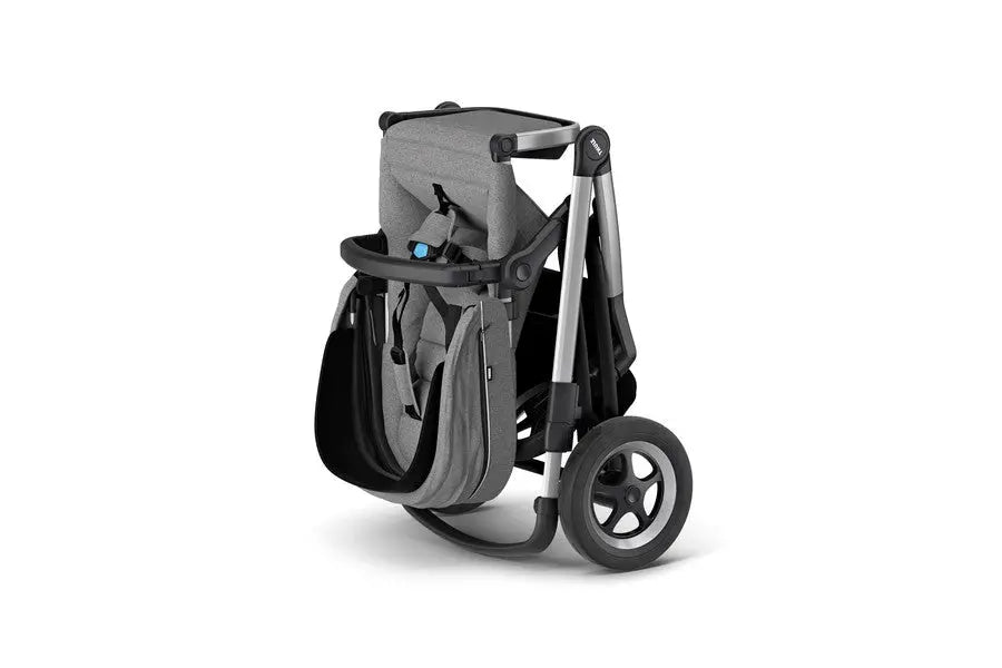 Thule Sleek Stroller in gray fabric with black frame, folded for compact storage, large rear wheels visible.