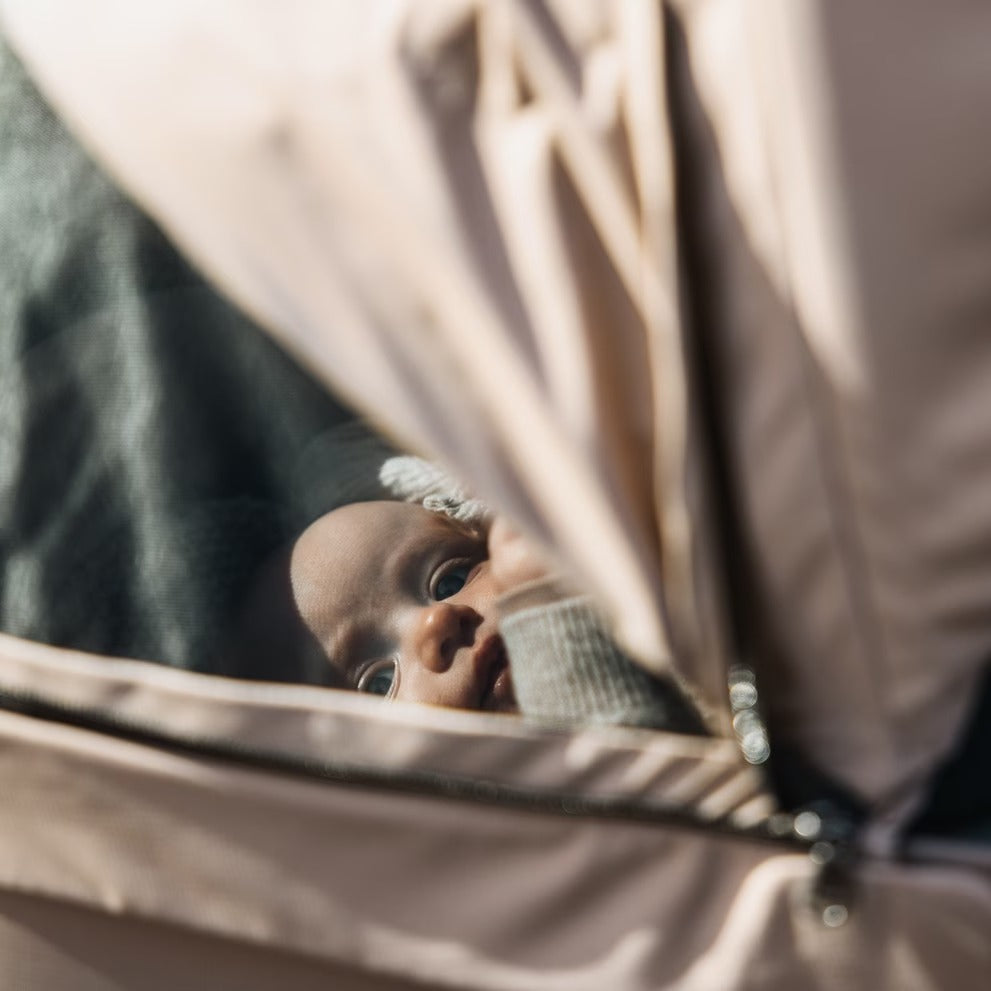 Thule Urban Glide 3 stroller, beige fabric, baby peering from the canopy window.
