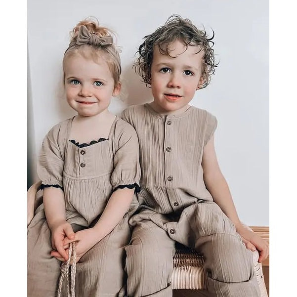 Turtledove London Herb Gauze Dress worn by a toddler girl beside a toddler boy in a matching beige romper.