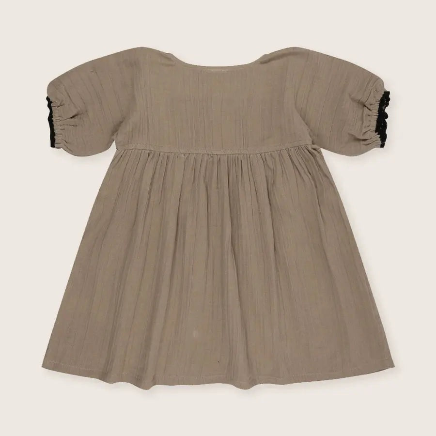Turtledove London Herb Gauze Dress for babies in taupe gauze with puff sleeves and black lace cuffs, laid flat.