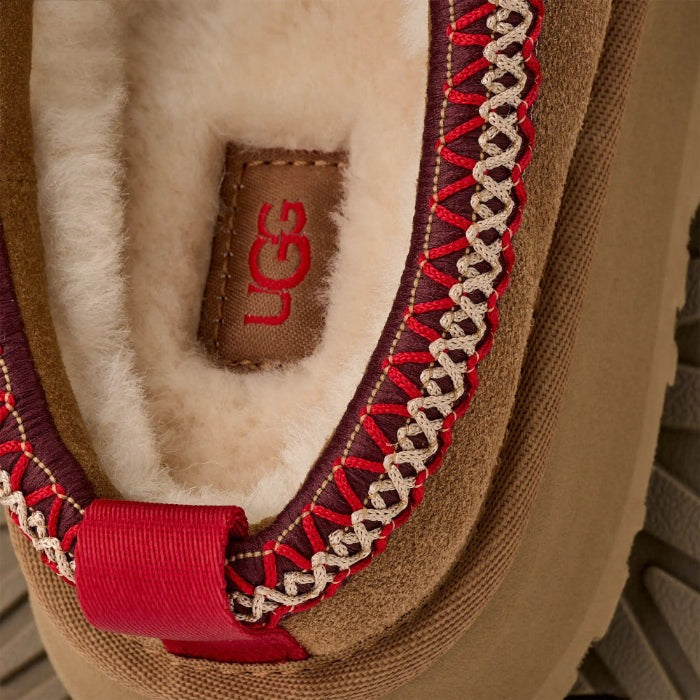 UGG Women's Tazz II Chestnut sandal with tan suede, cream shearling interior, and bold red stitch detail; logo tag visible.