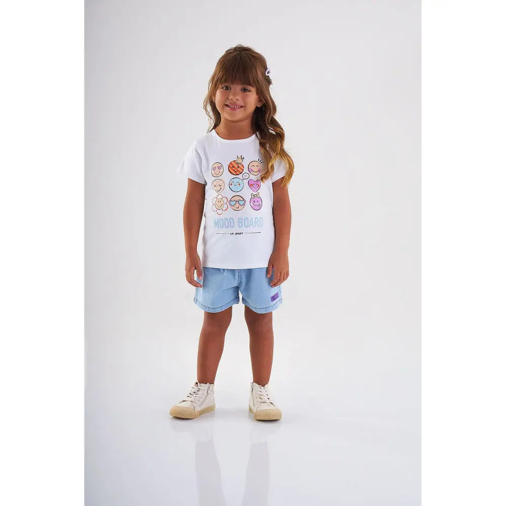 Up Baby Girl Short Sleeve Cotton Blouse White worn by a smiling girl in light blue shorts with emoji print.
