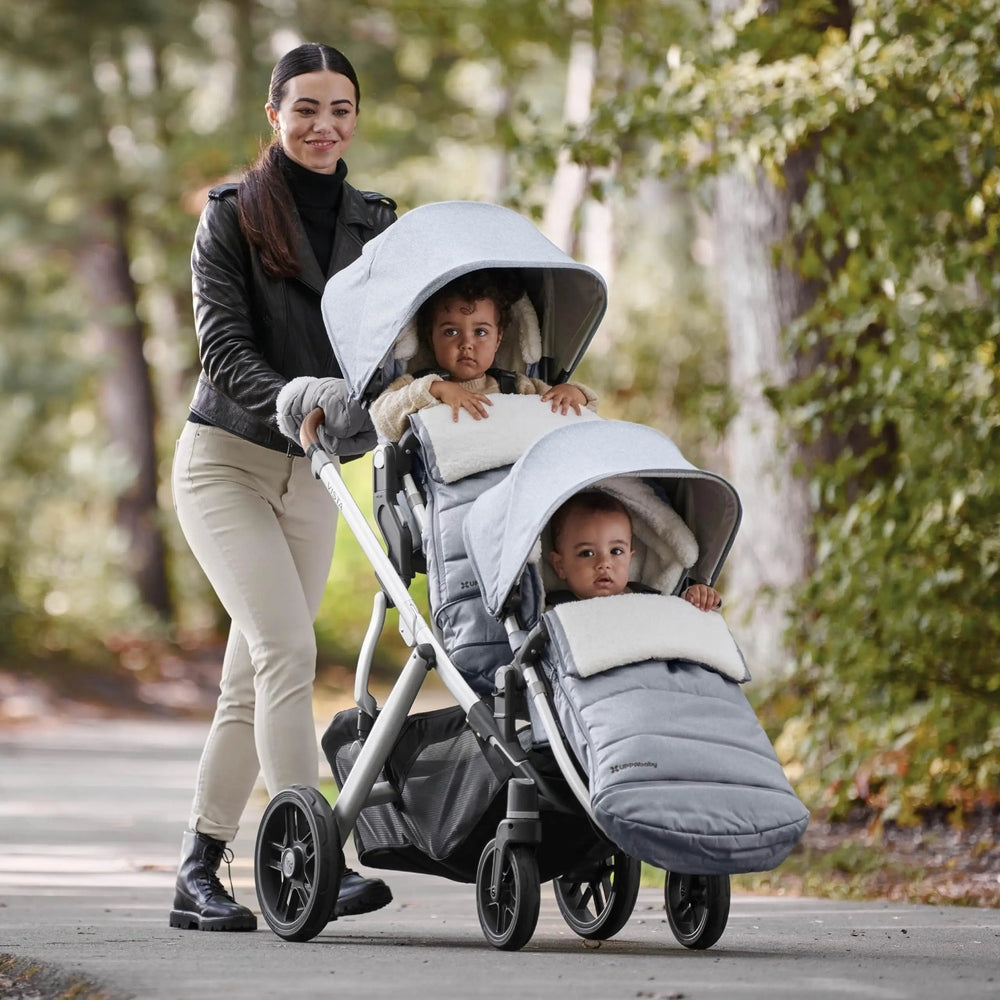 Uppababy Cozy Ganoosh gray stroller footmuffs on a double stroller as a mom pushes two infants outdoors.