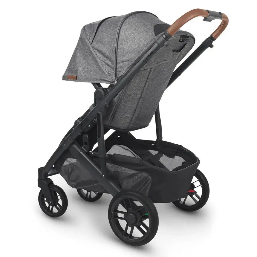 UPPAbaby Cruz V2 stroller in gray fabric with black frame and tan leather handle, bassinet attached and underseat storage.