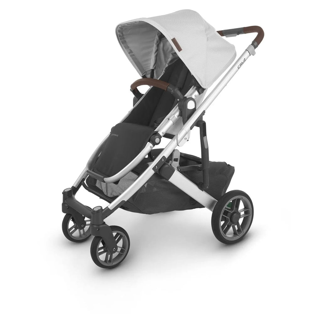 Uppababy Cruz V2 Stroller with silver frame, gray canopy, brown leather handlebar, and accessible storage basket.