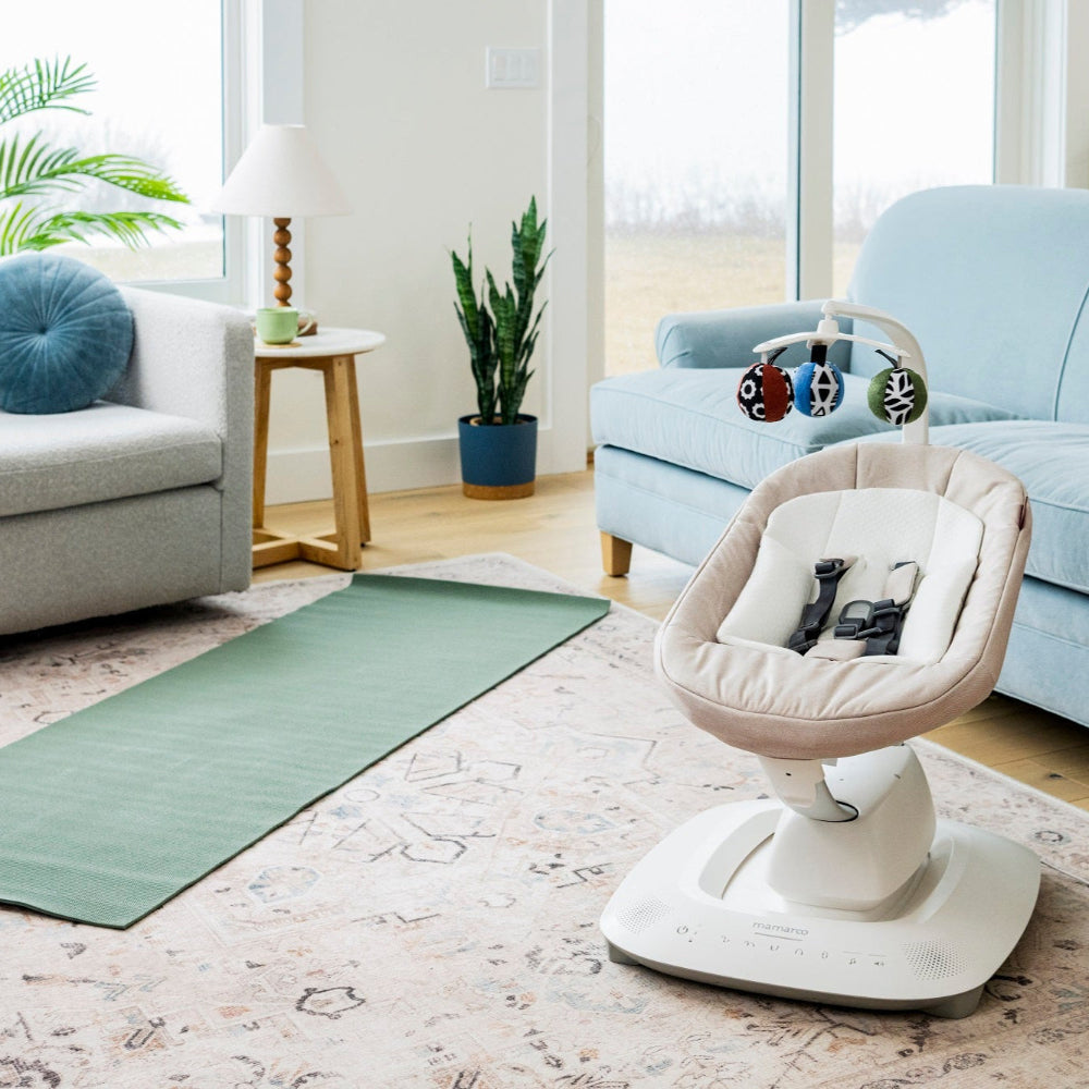 Uppababy Mamaroo Smart Swing in beige fabric with white base and colorful toy bar in a bright living room
