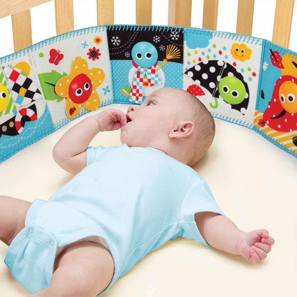 Yookidoo Lights N Music Baby Book surrounds a crib with bright padded panels as a baby lies on his back reaching.
