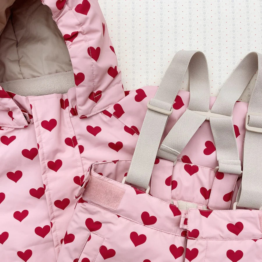 Konges Slojd Mismou Jacket Amour Pink heart-print coat with hood and soft lining, shown beside a beige backpack