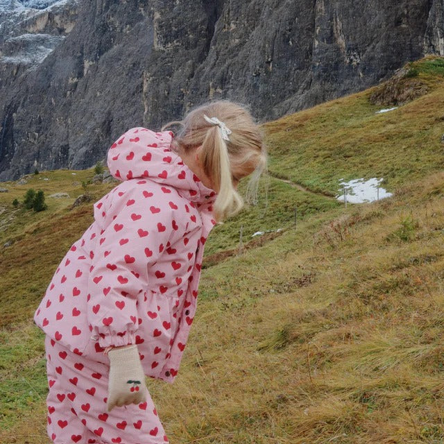 Konges Slojd Mismou Jacket Amour Pink worn by a child on a hillside, pink heart-print hooded outerwear.