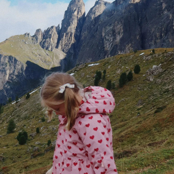 Konges Slojd Mismou Jacket Amour Pink hooded with red hearts worn by a girl in rugged mountain scenery.
