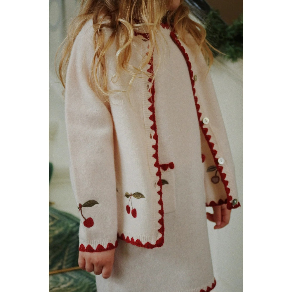 Konges Slojd Collette Cardigan Off White worn by a child, showing red zigzag trim, cherry embroidery and button front.