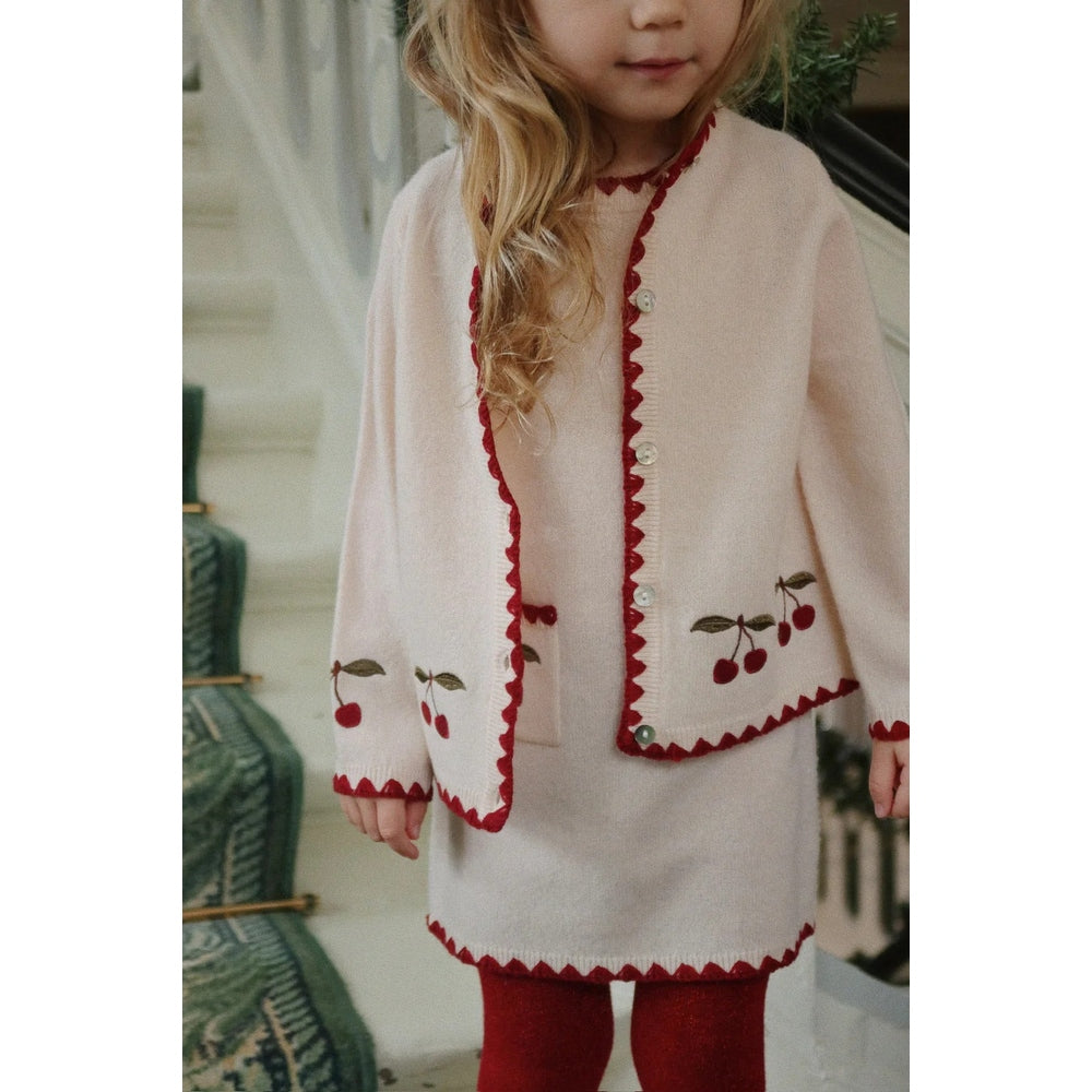 Konges Slojd Collette Cardigan Off White worn by a toddler, showing red scalloped trim, cherry embroidery, and white buttons.