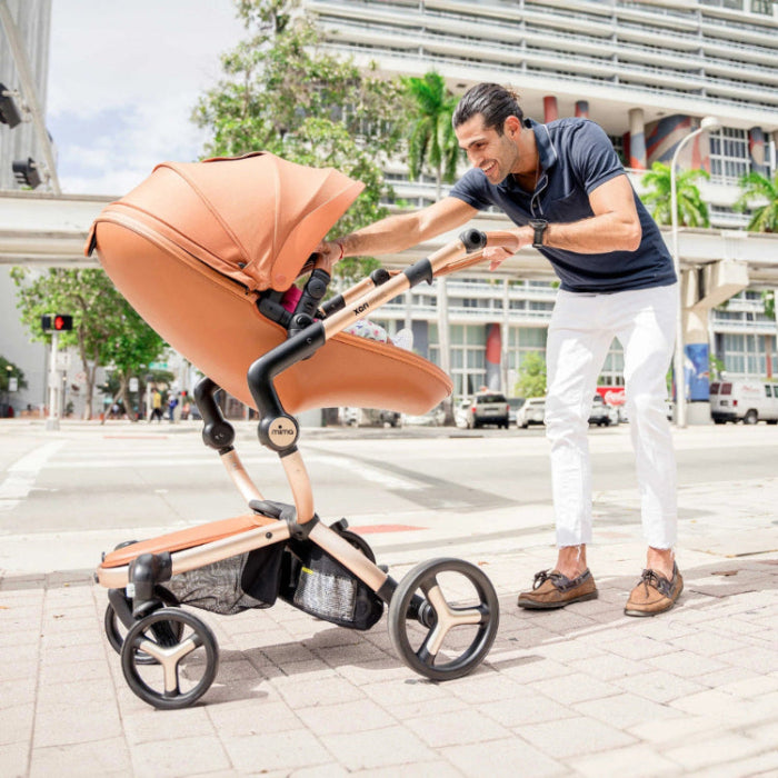 Mima Xari Max Stroller & Bassinet peach model, man pushing the bassinet-equipped stroller along a city street.
