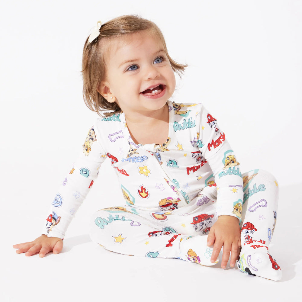 Bellabu Bear Playful Pups Bamboo Convertible Footie Paw Patrol; smiling toddler sits in white sleepwear with colorful prints.