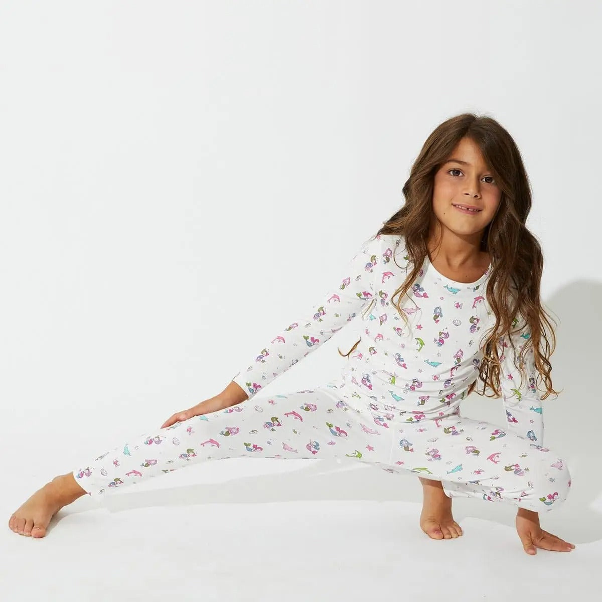 Bellabu Bear Bamboo Kids Pajamas Mermaid set in white with colorful mermaids, as a girl stretches in a pose.