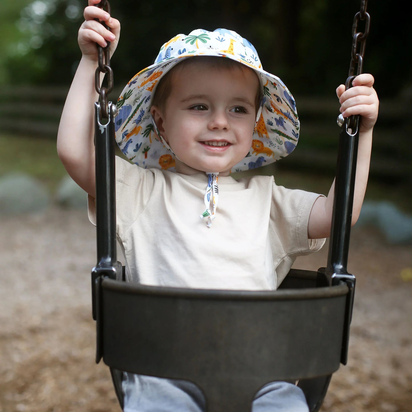JAN & JUL Kids Cotton Bucket Hat Safari worn by a smiling toddler on a swing.