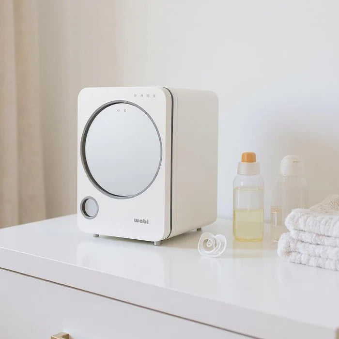 Wabibaby UVC LED Sanitizer & Dryer REV on a white dresser beside bottles and towels, featuring a circular front door.